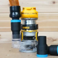 Black ToolCurve 1-1/4" hose adapter with blue band joining a vacuum hose to a DeWalt DCW600 trim router, plus a second adapter lying beside it