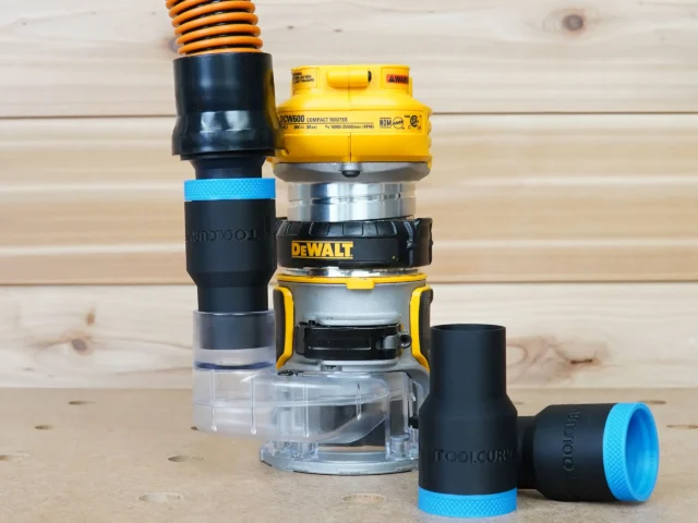 Black ToolCurve 1-1/4" hose adapter with blue band joining a vacuum hose to a DeWalt DCW600 trim router, plus a second adapter lying beside it
