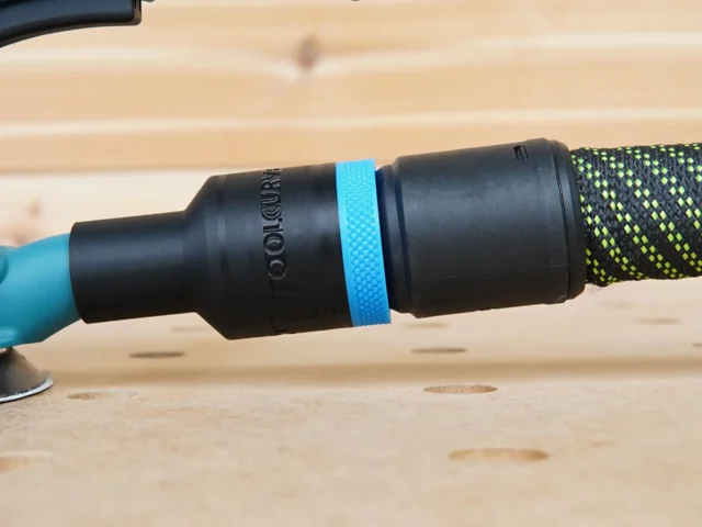 ToolCurve hose adapter attached to a Makita 5-inch sander, with blue band marking and black braided hose connected to the right port