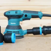 Black 1-1/4 inch ToolCurve hose adapter with blue band installed on a Makita 5in sander port, spare adapter beside it