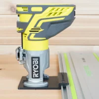 Ryobi trim router mounted on yellow and gray adapter, attached to a Kreg ACS guide rail on wooden workbench