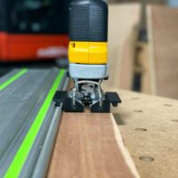 DeWalt jig saw adapter mounted on Festool track rail, showing black plastic base clamp and yellow control head attachment