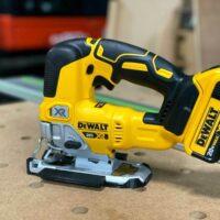 DeWalt 20V XR jig saw with yellow and black casing, positioned on a wood surface next to a green track rail