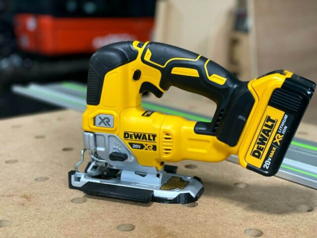 DeWalt 20V XR jig saw with yellow and black casing, positioned on a wood surface next to a green track rail