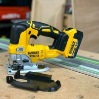 DeWalt 20V XR jig saw with black plastic rail adapter mounted to base, positioned next to Festool track on workbench