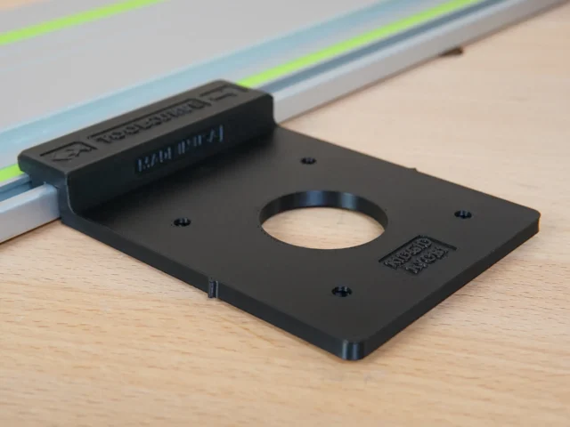Black plastic Ryobi trim router guide rail adapter mounted on a Festool track rail, showing a circular opening and mounting holes