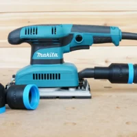 ToolCurve hose adapter for Makita sander with blue and black rubber connectors, shown alongside a Makita BO5030K orbital sander on wood