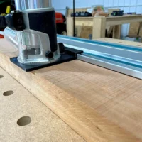 Makita trim router adapter mounted on wooden track with Festool guide rail, showing clear acrylic base and black mounting bracket