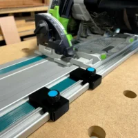 Two black limit stops with blue knurled knobs mounted on a Makita guide rail, positioned at different points along the track