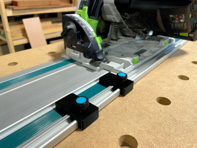 Two black limit stops with blue knurled knobs mounted on a Makita guide rail, positioned at different points along the track
