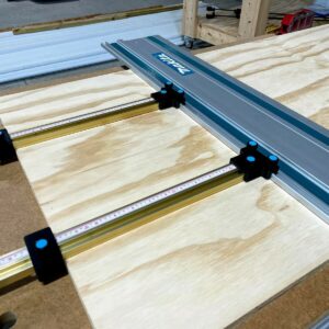 Black parallel guide brackets with blue knurled screws mounting Incra T-tracks to a Makita track saw rail over plywood