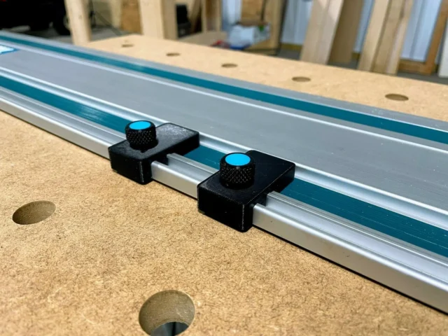 Two black 3D-printed limit stops mounted on a Makita track saw rail with blue knurled knobs for adjustment