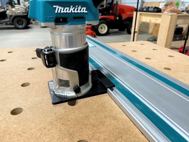 Makita trim router mounted on black adapter base, positioned next to blue guide rail on pegboard workbench