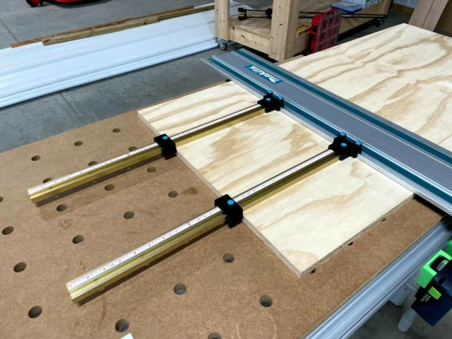Black ToolCurve parallel guide brackets mounted on brass T-tracks attached to a Makita track saw guide rail, positioned over a pegboard and wood workpieces