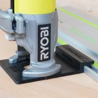 Ryobi trim router mounted on black adapter base attached to green guide rail on wooden workbench