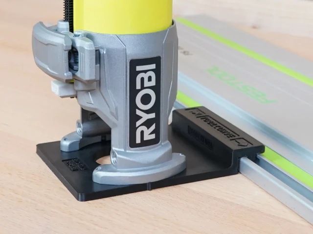 Ryobi trim router mounted on black adapter base attached to green guide rail on wooden workbench