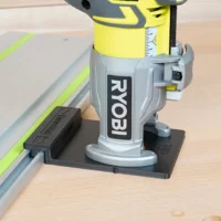 Ryobi trim router mounted on black adapter base, positioned on aluminum guide rail with yellow edge guide