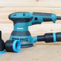 ToolCurve hose adapter with blue collar and black sleeve attached to Makita orbital sander, with two detached adapter sleeves on the surface