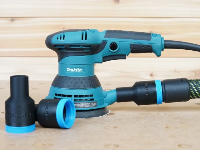 ToolCurve hose adapter with blue collar and black sleeve attached to Makita orbital sander, with two detached adapter sleeves on the surface
