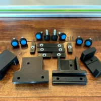 Parallel Guide system for Makita track saw displayed on wood, showing black brackets, spacers, knurled knobs with blue caps, and metal fasteners arranged flat