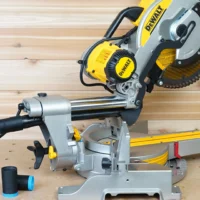 Black hose adapter with blue band joining a dust extractor hose to a DeWalt miter saw rear dust port, spare adapter alongside