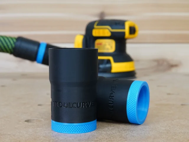 Black ToolCurve hose adapter with blue grip band, shown in foreground with a DeWalt sander blurred in the background