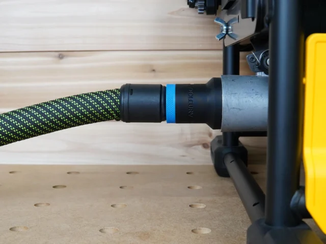 Black ToolCurve 27mm hose adapter with blue band joining a green vacuum hose to a DeWalt table saw dust port