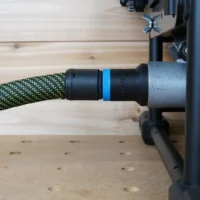 Black hose adapter with blue band attached to green-and-black braided dust hose, mounted on Dewalt table saw dust port