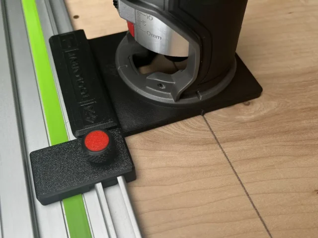 Milwaukee M18 router adapter mounted on a green guide rail, showing the black plastic base with red adjustment knob and measurement markings on the rail above