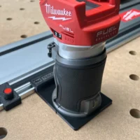 Milwaukee M18 trim router mounted on a blue FS rail using a black plastic adapter, shown on a pegboard work surface