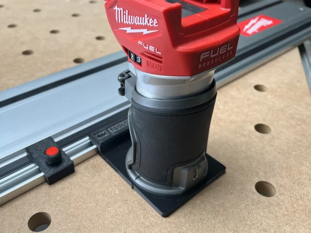 Milwaukee M18 trim router mounted on a blue FS rail using a black plastic adapter, shown on a pegboard work surface