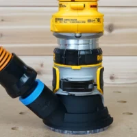 Blue hose adapter cover attached to DeWalt DCW600 compact router base with orange dust hose connected