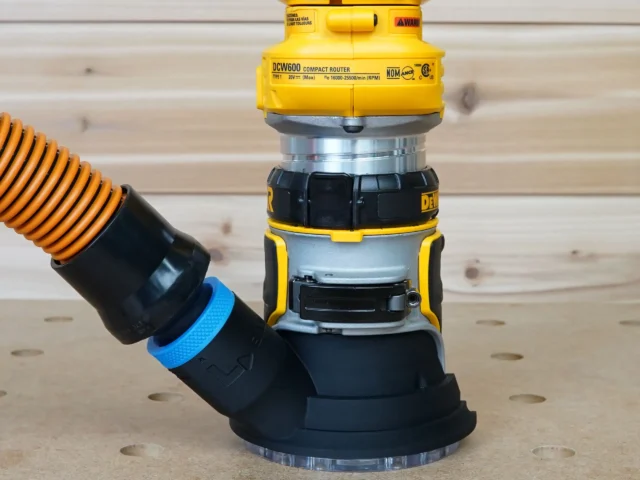 Blue hose adapter cover attached to DeWalt DCW600 compact router base with orange dust hose connected