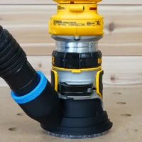Black hose adapter with blue grip ring attached to DeWalt DCW600 compact router, with black corrugated hose connected to adapter inlet