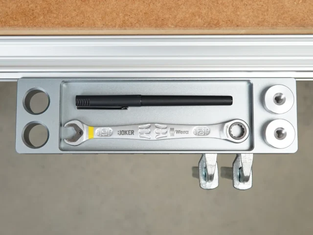 Aluminum utility rack mounted on workbench profile with two bench dogs, pen holder, and Wera wrench displayed inside