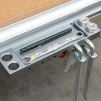 Aluminum utility rack mounted on Festool MFT/3 workbench t-track, holding quick clamps, bench dogs, and tools with two threaded mounting points visible at top