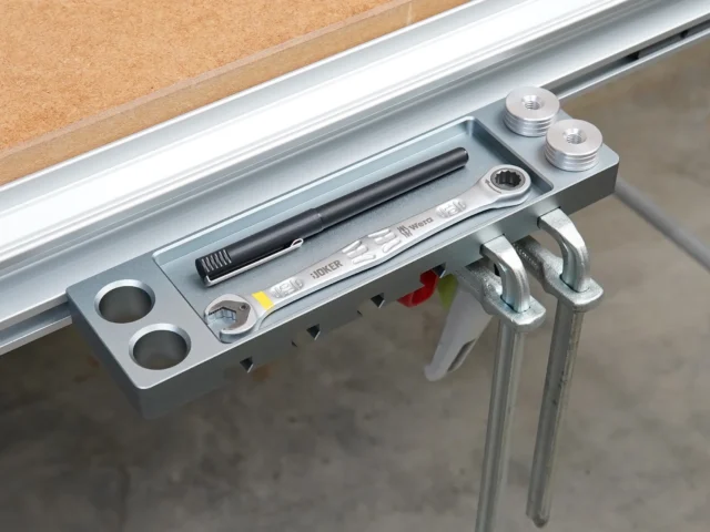 Aluminum utility rack mounted on Festool MFT/3 workbench t-track, holding quick clamps, bench dogs, and tools with two threaded mounting points visible at top