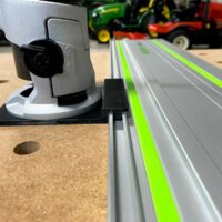 Bosch Colt router mounted on gray adapter base, attached to Festool-style aluminum guide rail with green stripe