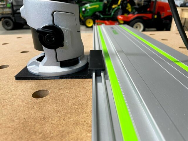 Bosch Colt router mounted on gray adapter base, attached to Festool-style aluminum guide rail with green stripe