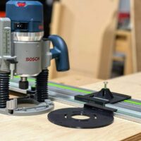 Bosch 1617 plunge router mounted on FS rail with black LR32 drilling plate and spring-loaded depth stop positioned for hole drilling