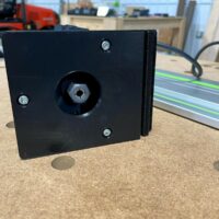 Black 3D-printed adapter with threaded center post and mounting holes, positioned next to a Festool guide rail on a workbench