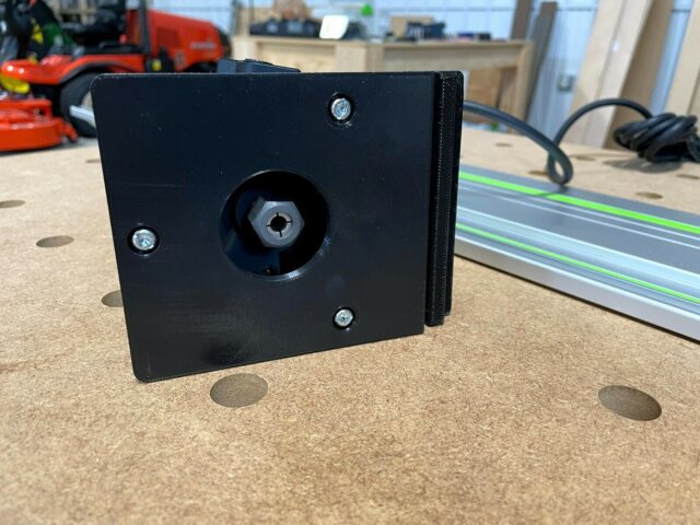 Black 3D-printed adapter with threaded center post and mounting holes, positioned next to a Festool guide rail on a workbench