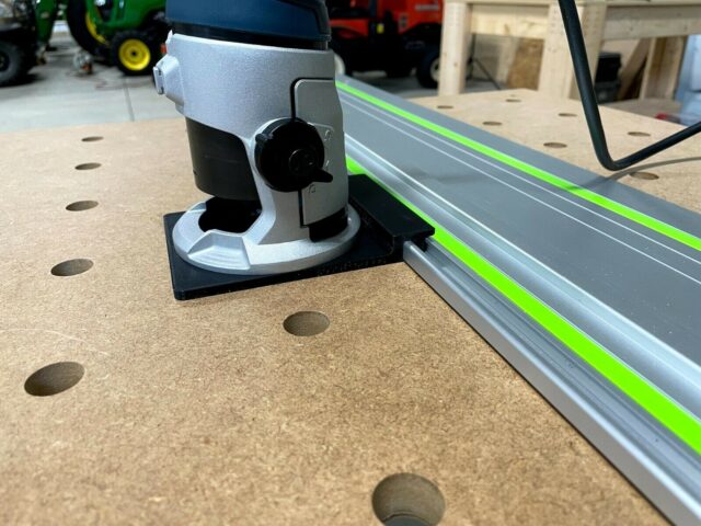 Bosch Colt router adapter mounted on black base plate, positioned beside a Festool guide rail on perforated work surface