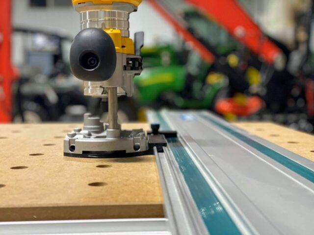 Dewalt DNP612 router adapter mounted on Makita guide rail, showing black wheel and metal base connected to the track