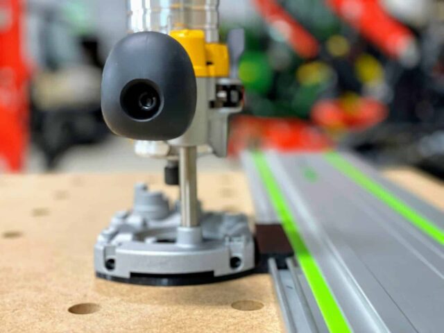 Black guide rail adapter mounted on a Dewalt trim router base, positioned on a Festool track with green edge guide stripe
