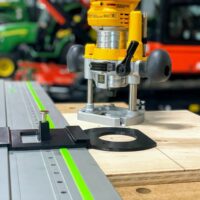 Dewalt plunge router mounted on aluminum track rail with black ToolCurve LR32 adapter plate and spring-loaded knob positioned on wooden workpiece