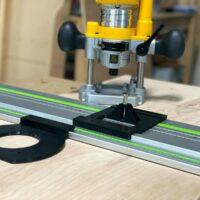 Dewalt trim plunge router mounted on Festool rail with ToolCurve LR 32 plate and black drilling jig attached to rail, showing circular base plate and guide stops