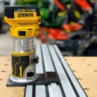 DeWalt trim router mounted on black adapter plate positioned over DeWalt guide rail track on pegboard workbench