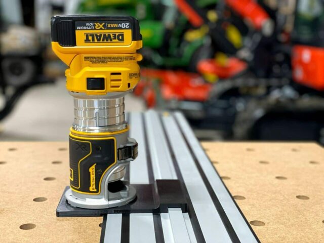 DeWalt trim router mounted on black adapter plate positioned over DeWalt guide rail track on pegboard workbench
