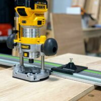 DeWalt trim plunge router mounted on aluminum guide rail with ToolCurve LR32 plate and spring-loaded knob attached to base